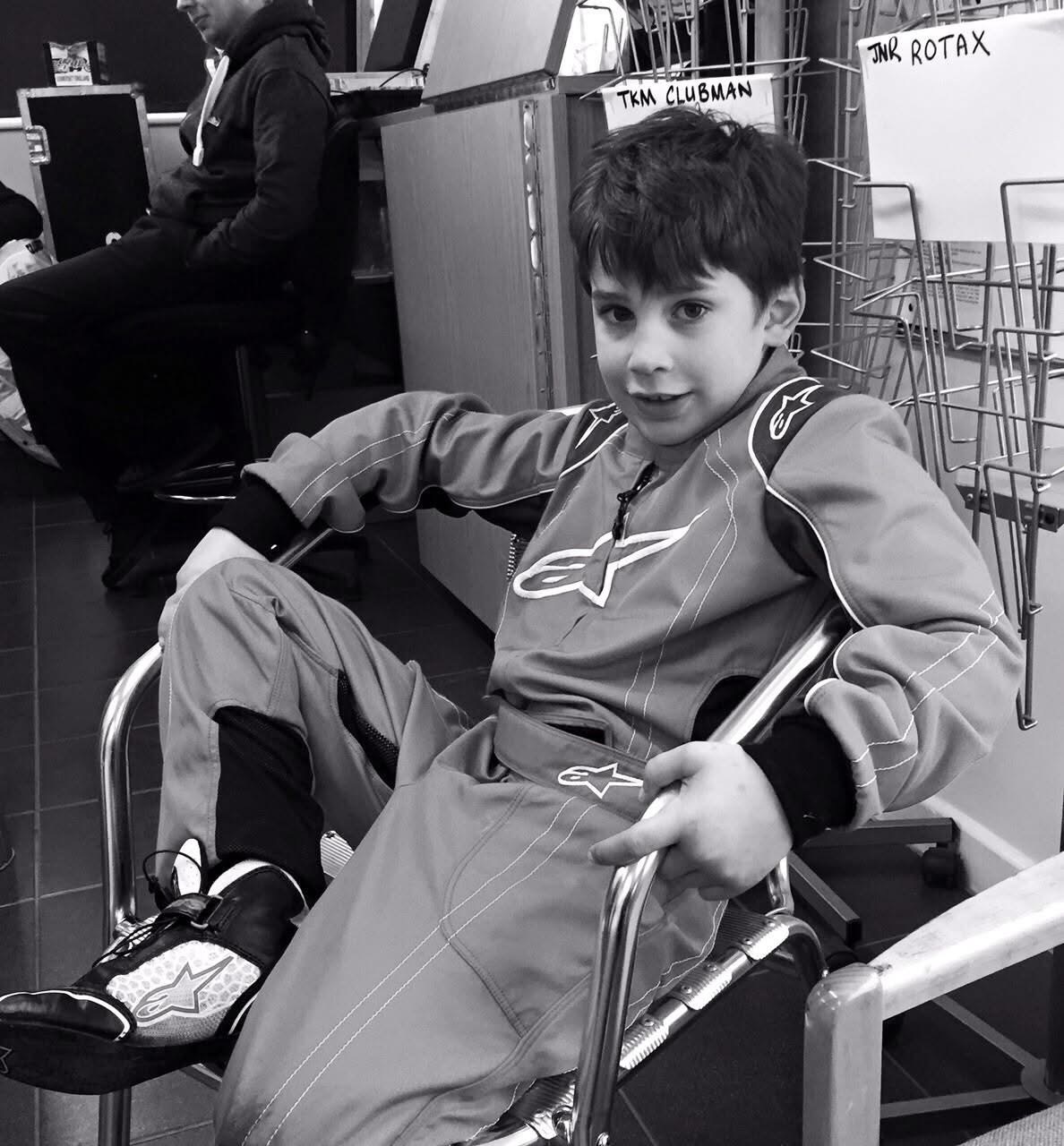 Christian Valverde as a young boy in his race suit, sitting in a chair