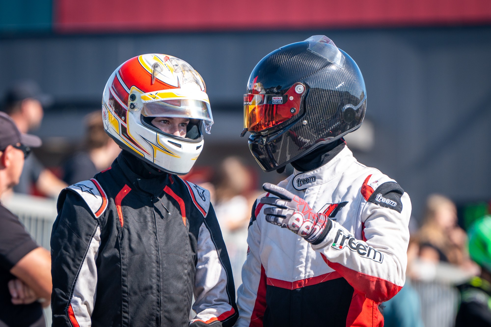 Two karting drivers in helmets talking in the paddock