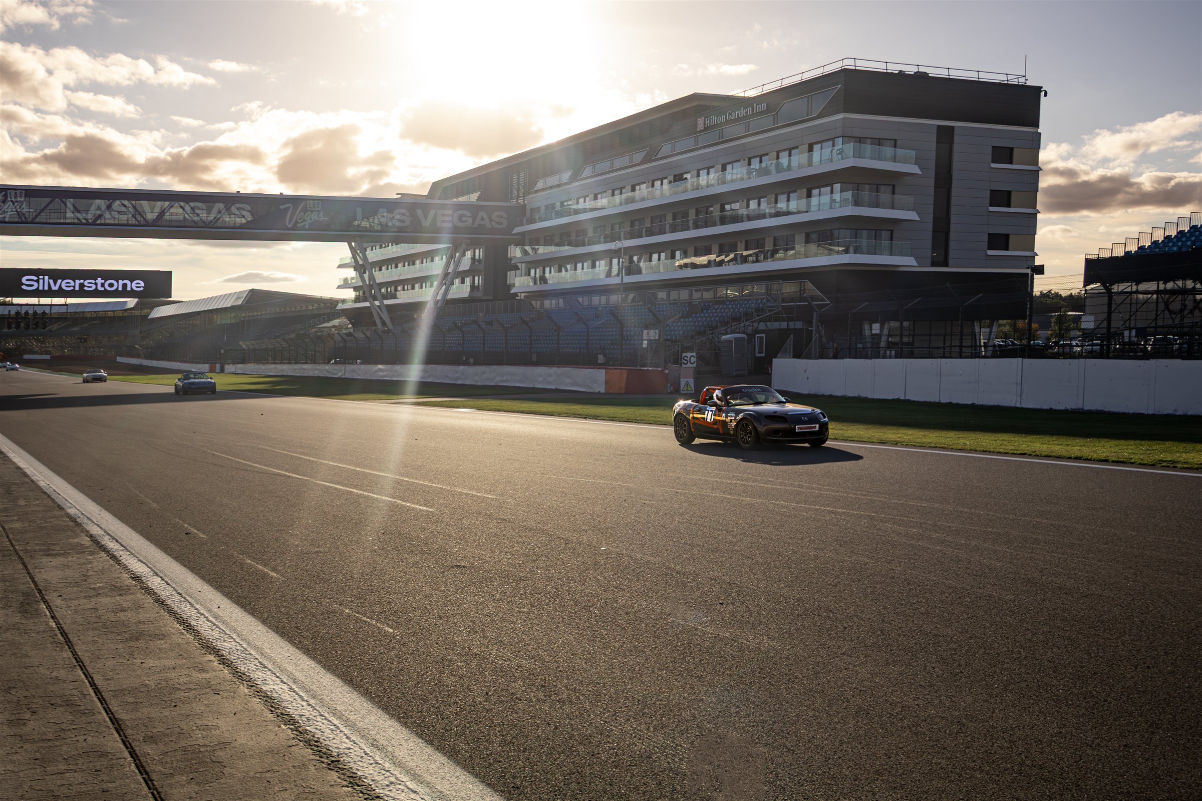 The MX-5 on track at Silverstone, with the sun behind the hotel