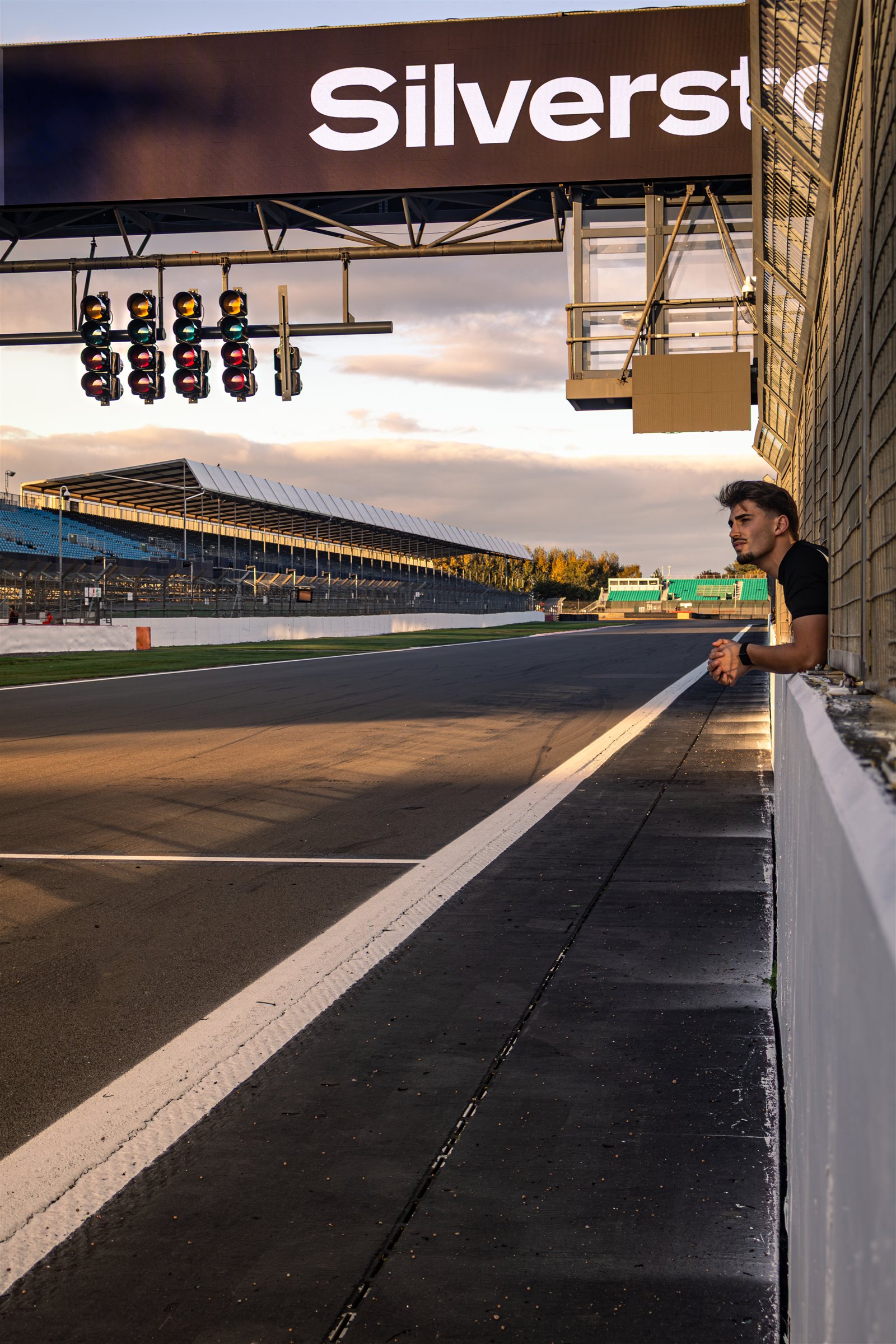 Christian Valverde leaning over the pit wall at Silverstone, under the Silverstone sign and the start lights
